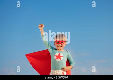 Superheld Kind spielt draußen. Super Held Kind vor blauem Sommerhimmel Hintergrund. Vorstellung und Freiheit Konzept Stockfoto