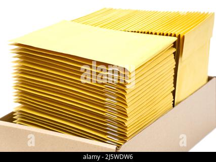 Zwei Stapel gelber Umschläge in einem auf Weiß isolierten Kraftkarton. Büromaterial. Stockfoto