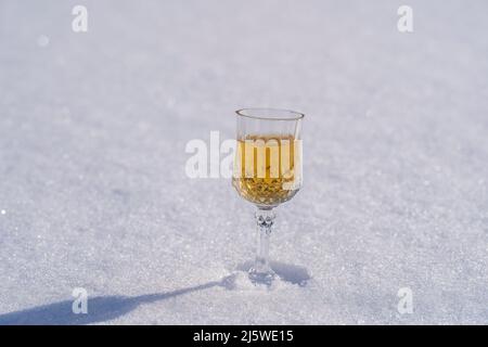 Hausgemachte Fruchttinktur in einem Weinkristallglas auf einem Schnee und weißem Hintergrund im Winter, Ukraine, Nahaufnahme. Berry alkoholische Getränke Konzept Stockfoto