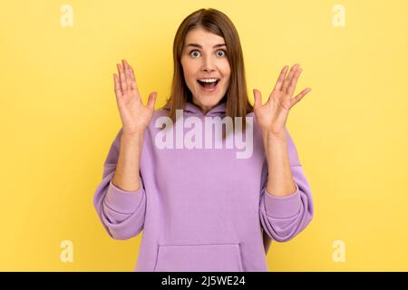 Oh mein gott, wow. Porträt einer überraschten Frau, die mit offenem Mund erstaunt auf die Kamera schaut, Schock, Erstaunen ausdrückt und einen purpurnen Hoodie trägt. Innenaufnahme des Studios isoliert auf gelbem Hintergrund. Stockfoto