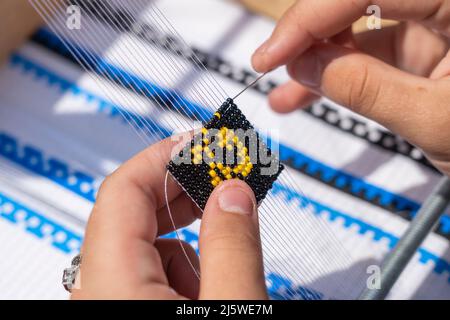 Junges Mädchen macht ein Armband mit Perlen mit ihren Händen, Ukraine, Nahaufnahme. Elemente der Stickerei aus Perlen, Gemälde und handgemachte von Meistern von Perlen Stockfoto