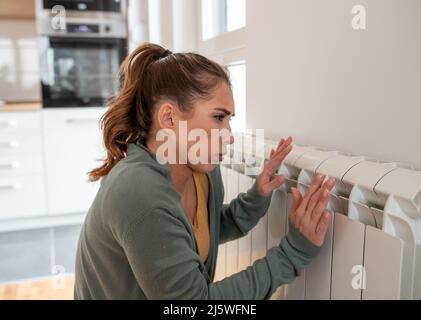 Frau, die sich kalt fühlte, wärmte ihre Hände in der Nähe des Heizkörpers zu Hause. Stockfoto