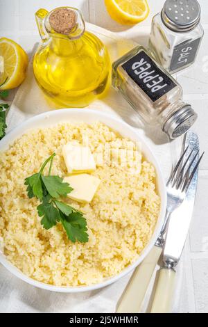 Gekochter Couscous mit Koriander oder Petersilie, Butter, Olivenöl, Zitrone in weißer Keramikschale auf weißem Küchentisch Kopierplatz Stockfoto