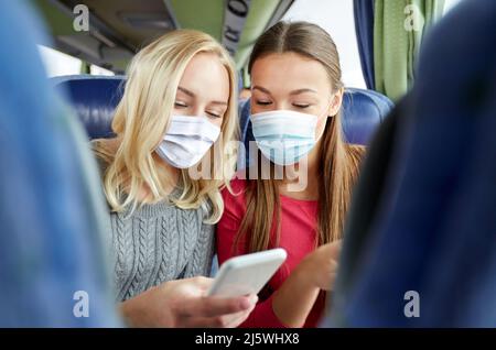 Frauen in Masken im Reisebus mit Smartphone Stockfoto