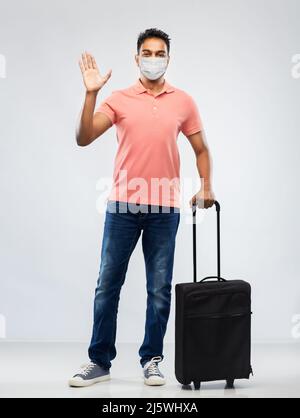 indischer Mann in Maske mit Reisetasche winkende Hand Stockfoto