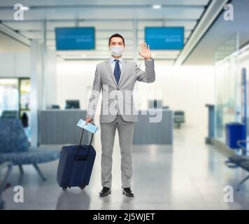 Geschäftsmann in Maske mit Reisetasche am Flughafen Stockfoto