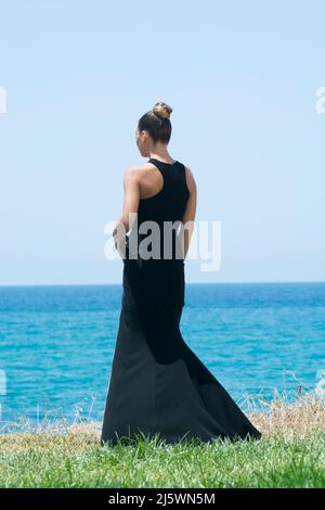 Rückansicht einer jungen Frau in schwarzem Kleid, die am Strand steht Stockfoto