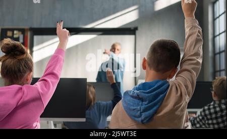 Rückansicht von Schulkindern, die während der Computerverkalkung in der Schule die Hände heben. Stockfoto
