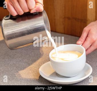 Gieße heiße, schaumige Milch in einen Kaffee, um einen Latte zu machen Stockfoto