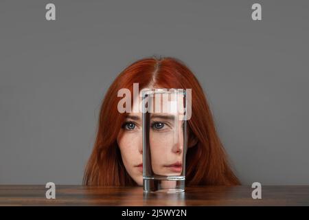 Verzerrtes Gesicht einer Frau, die durch ein Glas Wasser schaut Stockfoto