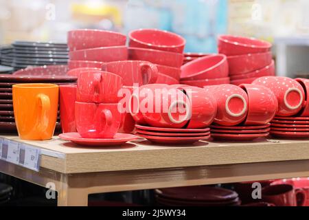 Сups werden im Laden verkauft. Reihen von verschiedenen roten Tassen für zu Hause auf Regalen in einem Supermarkt. Stockfoto