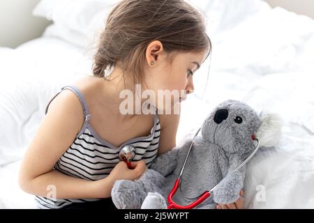 Glückliches kleines Mädchen mit weichem Spielzeug Koala im Bett. Stockfoto