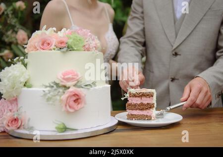 Unverkennbares Brautpaar, das am Hochzeitstag den Kuchen zerschneidet Stockfoto