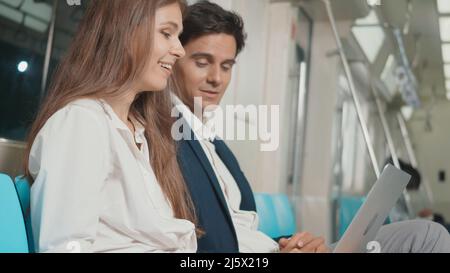 Junge kaukasische weiße Geschäftsfrau und Mann, die mit einem Laptop sitzen Computer arbeitet zusammen im Gespräch auf der U-Bahn-Zug in der Morgen während des Ausgehend zu Stockfoto