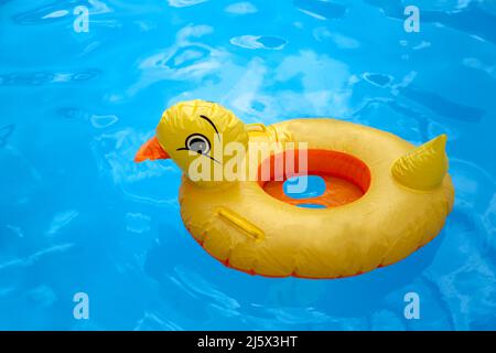 Gelbes aufblasbares Duckling Spielzeug aus Kunststoff im blauen Pool mit Wasser Stockfoto