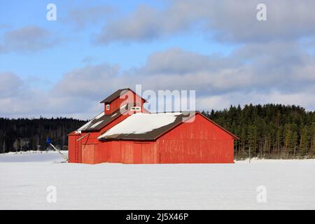 Roter, alter Holzkorntrockner im Feld an einem klaren Tag im Februar mit schneebedecktem Feld und blauem Himmel und Wolken. Stockfoto