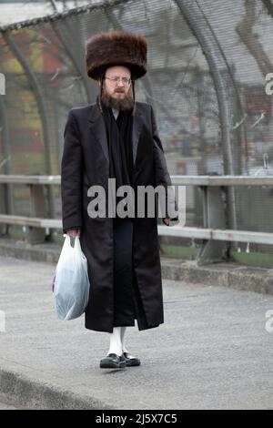 Auf Passah und in langen weißen Strümpfen und einem Shtreimel-Pelzhut geht ein orthodoxer jüdischer Mann mit einer Einkaufstasche spazieren. In Williamsburg, Bklyn, NYC Stockfoto