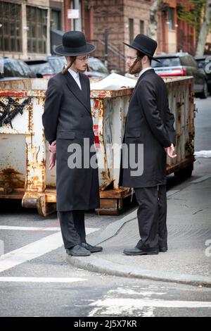 Zwei orthodoxe jüdische junge Männer mit ähnlichen Posen und ähnlichen Kleidern unterhalten sich auf der Lee Avenue in williamsburg, Brooklyn, New York City. Stockfoto