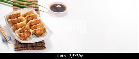 Taiwanesisches und japanisches gebratenes Gyoza-Knödel-Jiaozi-Essen auf einem Teller mit Sojasauce auf weißem Tischhintergrund. Stockfoto