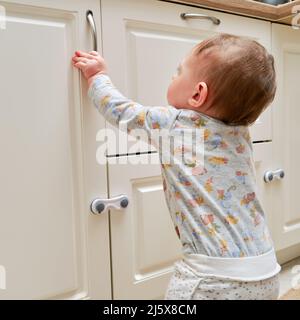 Kleinkind Baby Junge reißt aus einem Schrank Schublade mit seiner Hand. Das Kind hält den Schranktürgriff, kleines Kind Stockfoto