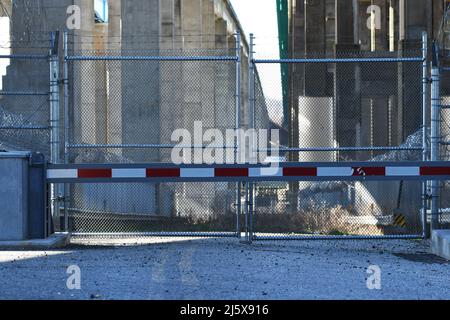 KEIN ZUGANG: Eine Straße zu einem Industriekomplex unter einer Autobahn, die von Stacheldraht umgeben ist und auf dem wildes Gras wächst, ist gesperrt und eingezäunt. Stockfoto