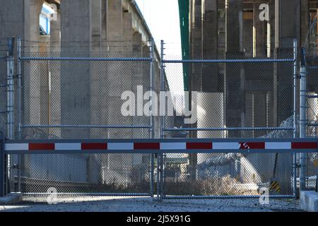 KEIN ZUGANG: Eine Straße zu einem Industriekomplex unter einer Autobahn, die von Stacheldraht umgeben ist und auf dem wildes Gras wächst, ist gesperrt und eingezäunt. Stockfoto