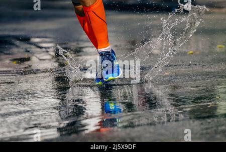 Beine männlicher Sportler läuft Pfütze. Wasserspritzer Stockfoto