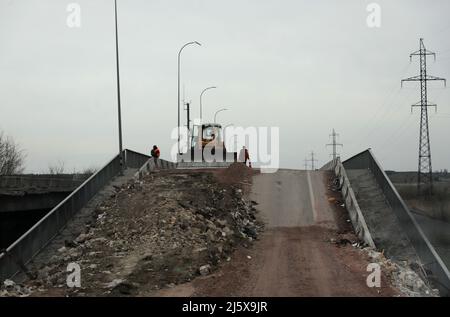 BORODIANKA, UKRAINE - 26. APRIL 2022 - Arbeiter flankieren einen Bulldozer auf einer Brücke, die als Folge der russischen Invasion zerstört wurde, Borodianka, Region Kiew, n Stockfoto