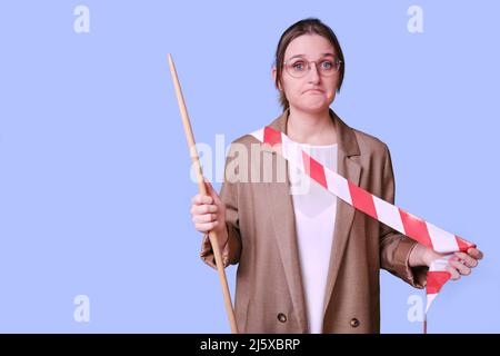 Traurige Lehrerin hält ein rot-weißes Band auf einem blauen Hintergrund im Studio, Kopierraum Stockfoto