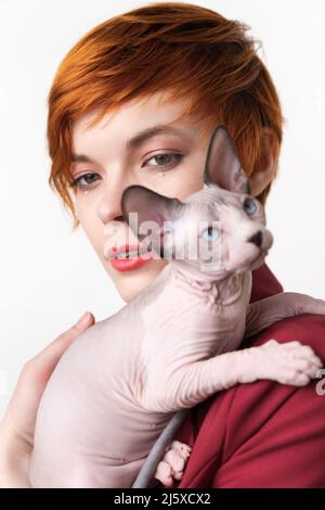 Die Kanadierin Sphynx Cat schaut weg und sitzt auf der Schulter einer rothaarige junge Frau. Selektiver Fokus auf heimische, haarlose Jungtiere im Vordergrund Stockfoto