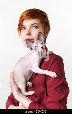 Kanadische Sphynx Katze sitzt auf der Schulter einer jungen Hipster-Rotschopf-Frau. Selektiver Fokus auf heimische Jungtiere im Vordergrund, geringe Schärfentiefe Stockfoto