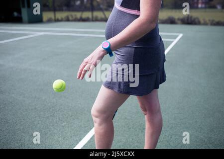 Eine Schwangerin hüpft auf dem Tennisplatz den Tennisball Stockfoto