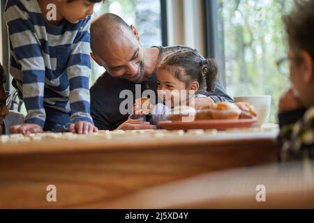 Glücklicher Vater und Tochter essen Muffin am Esstisch Stockfoto