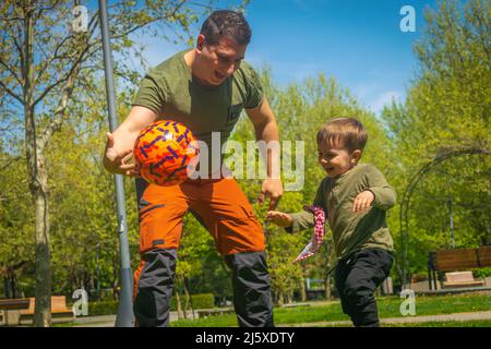 Vater und Sohn spielen Fußball im Park Outdoor Familienaktivitäten Fußball Fans Fans Fans wärmen sich für die Qatar World Cup 2022 Vater und Sohn spielen ama Stockfoto