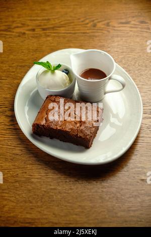 Schokoladenkuchen auf einem Holztisch mit Eis und Minzblatt auf der Oberseite, Restaurantkarte Stockfoto