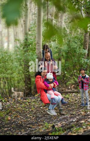 Verspielte Familie auf Schaukel im Wald Stockfoto