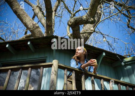 Lächelnde junge Frau, die Kaffee auf dem Balkon des Baumhauses trinkt Stockfoto