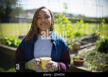 Porträt lächelnde junge Frau, die im sonnigen Garten Tee trinkt Stockfoto