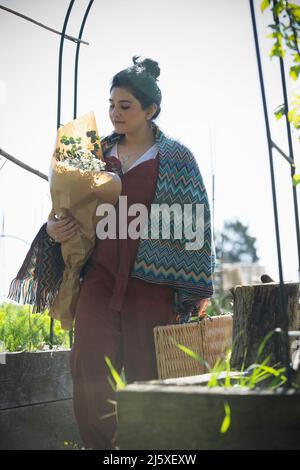 Junge Frau mit Blumenstrauß und Picknickkorb im sonnigen Garten Stockfoto