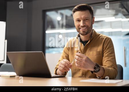 Glücklicher Geschäftsmann, Der In Der Nähe Eines Laptops Sitzt Und Im Büro Arbeitet Stockfoto