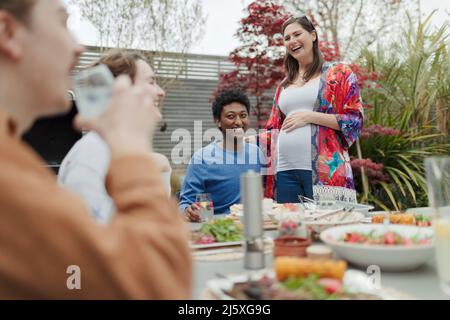 Glückliches, trächtiges Paar, das mit Freunden auf der Terrasse zu Mittag essen kann Stockfoto