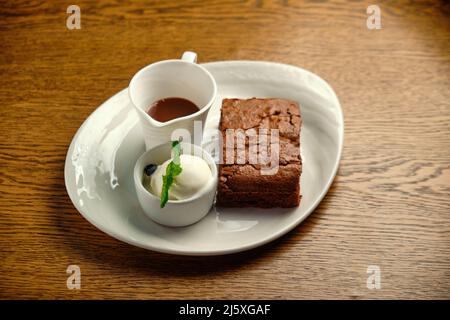 Schokoladenkuchen auf einem Holztisch mit Eis und Minzblatt auf der Oberseite, Restaurantkarte Stockfoto