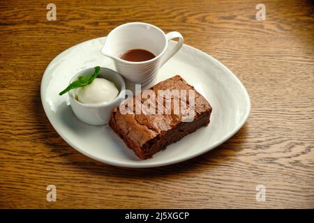 Schokoladenkuchen auf einem Holztisch mit Eis und Minzblatt auf der Oberseite, Restaurantkarte Stockfoto