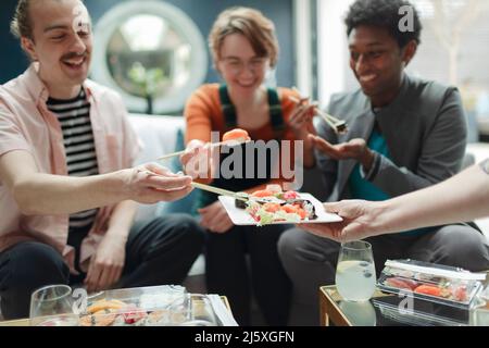Glückliche Freunde, die Sushi zum Mitnehmen im Wohnzimmer teilen Stockfoto