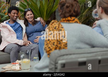 Ein trächtiges Paar, das mit Freunden auf der Terrasse rumhängt Stockfoto