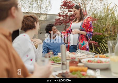 Glückliches, trächtiges Paar, das mit Freunden am Tisch auf der Terrasse zu Mittag essen kann Stockfoto