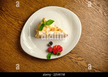 Kuchen mit Napoleon-Creme auflegen auf einem weißen Teller mit Erdbeeren auf einem Holztisch aufschlagen Stockfoto