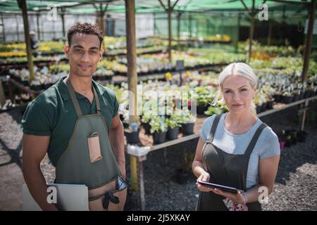 Portrait selbstbewusste Pflanzenzügnerinnen im sonnigen Gewächshaus Stockfoto