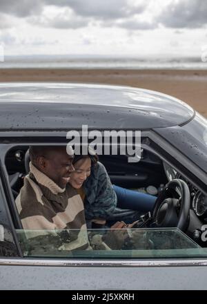 Glückliches Paar mit Smartphone im Auto am Winterstrand Stockfoto