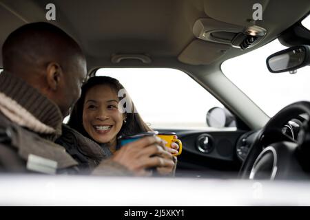 Glückliches Paar trinkt Kaffee im Auto Stockfoto